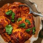 A casserole dish with baked chicken thighs coated in a tomato sauce.