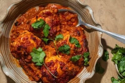 A casserole dish with baked chicken thighs coated in a tomato sauce.