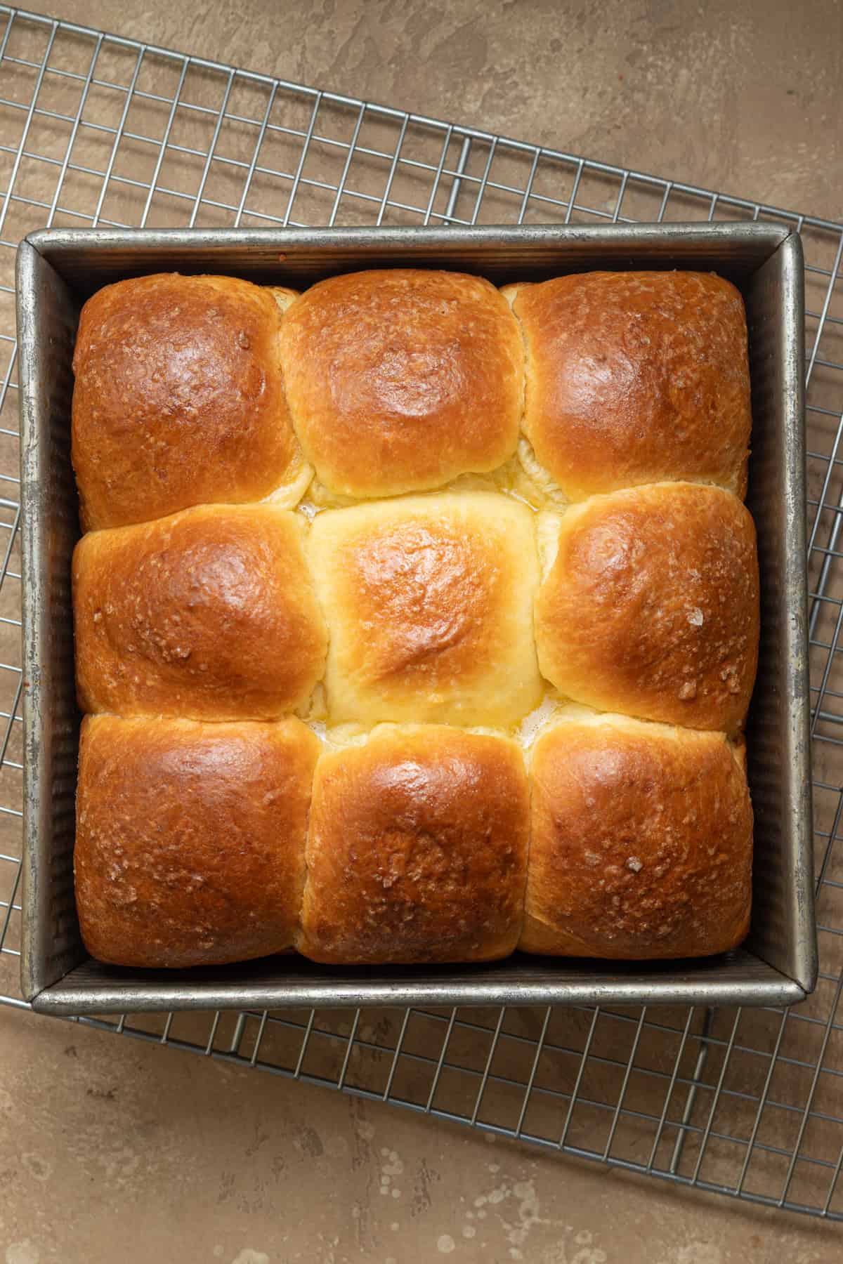 Brioche rolls in a metal baking pan on a wire rack.