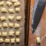 Ricotta gnocchi on a baking sheet next to a cutting board with more gnocchi and a knife.