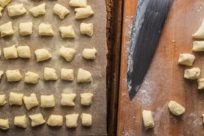 Ricotta gnocchi on a baking sheet next to a cutting board with more gnocchi and a knife.