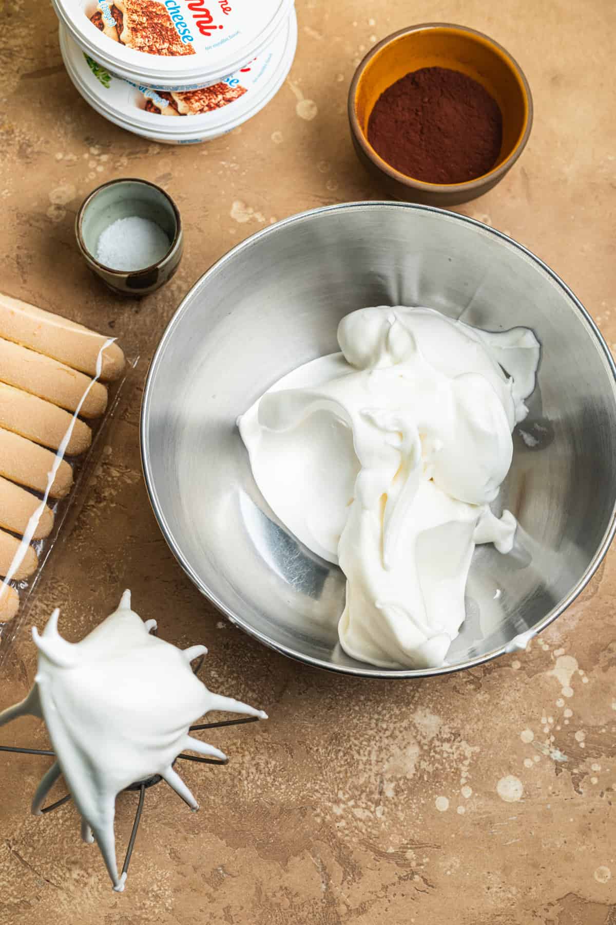 A bowl of whipped egg whites with various ingredients in the background.
