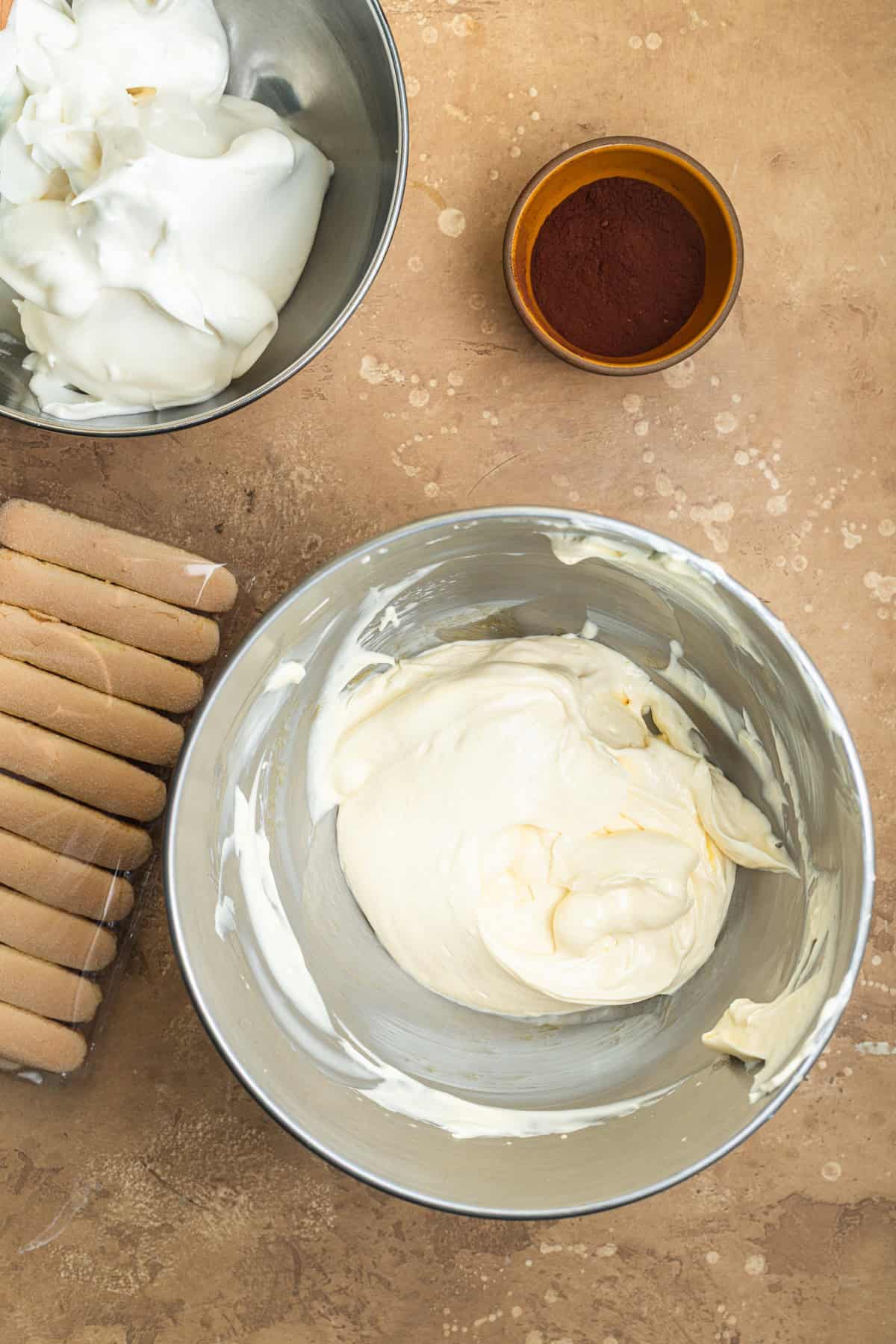 A bowl of whipped egg yolks and mascarpone with a bowl of whipped egg whites in the background.