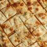 Focaccia di Recco on a wooden peel cut into individual squares.