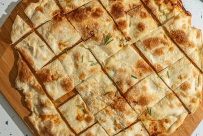 Focaccia di Recco on a wooden peel cut into individual squares.