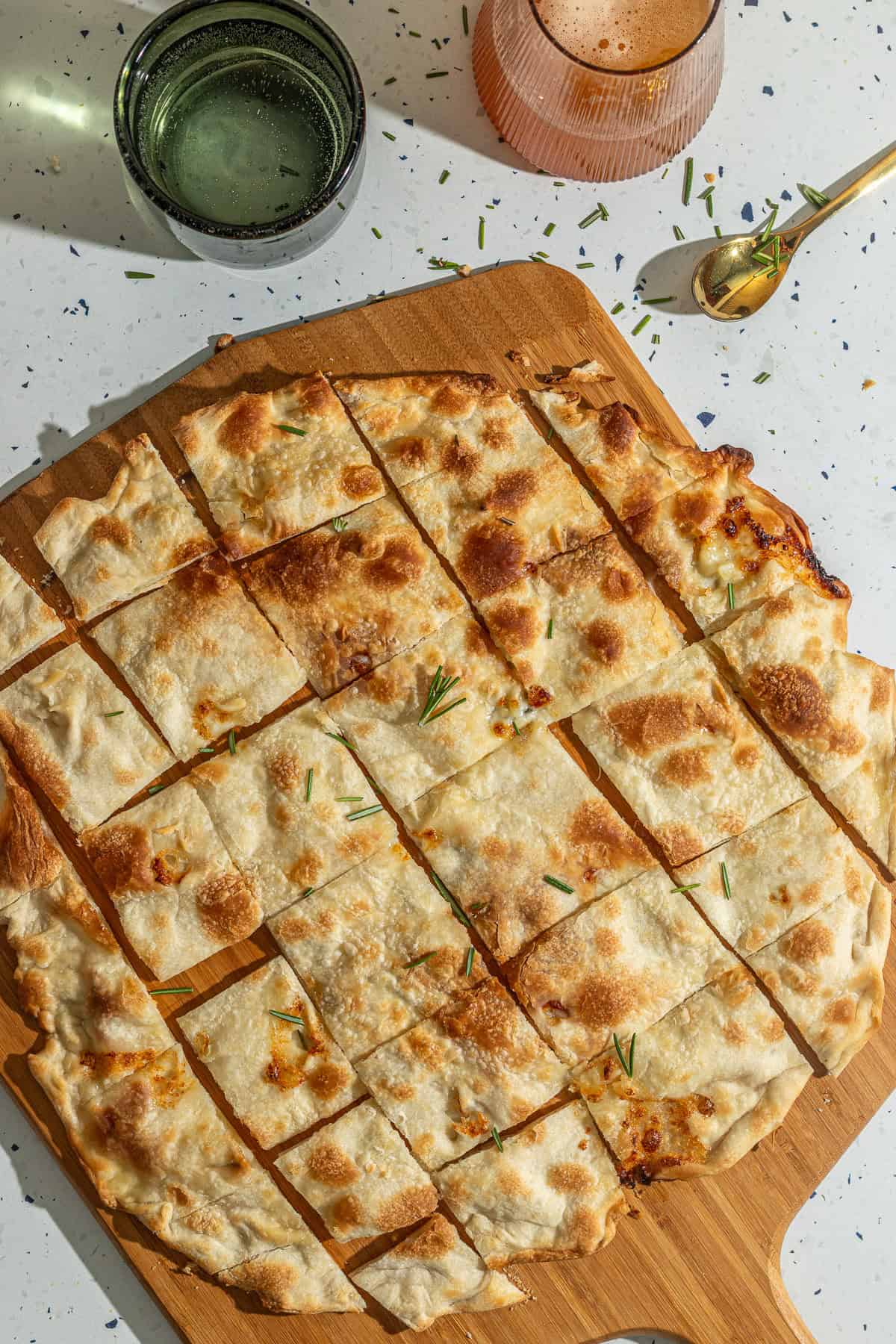 Slices of focaccia di recco on a pizza peel with glasses in the background.