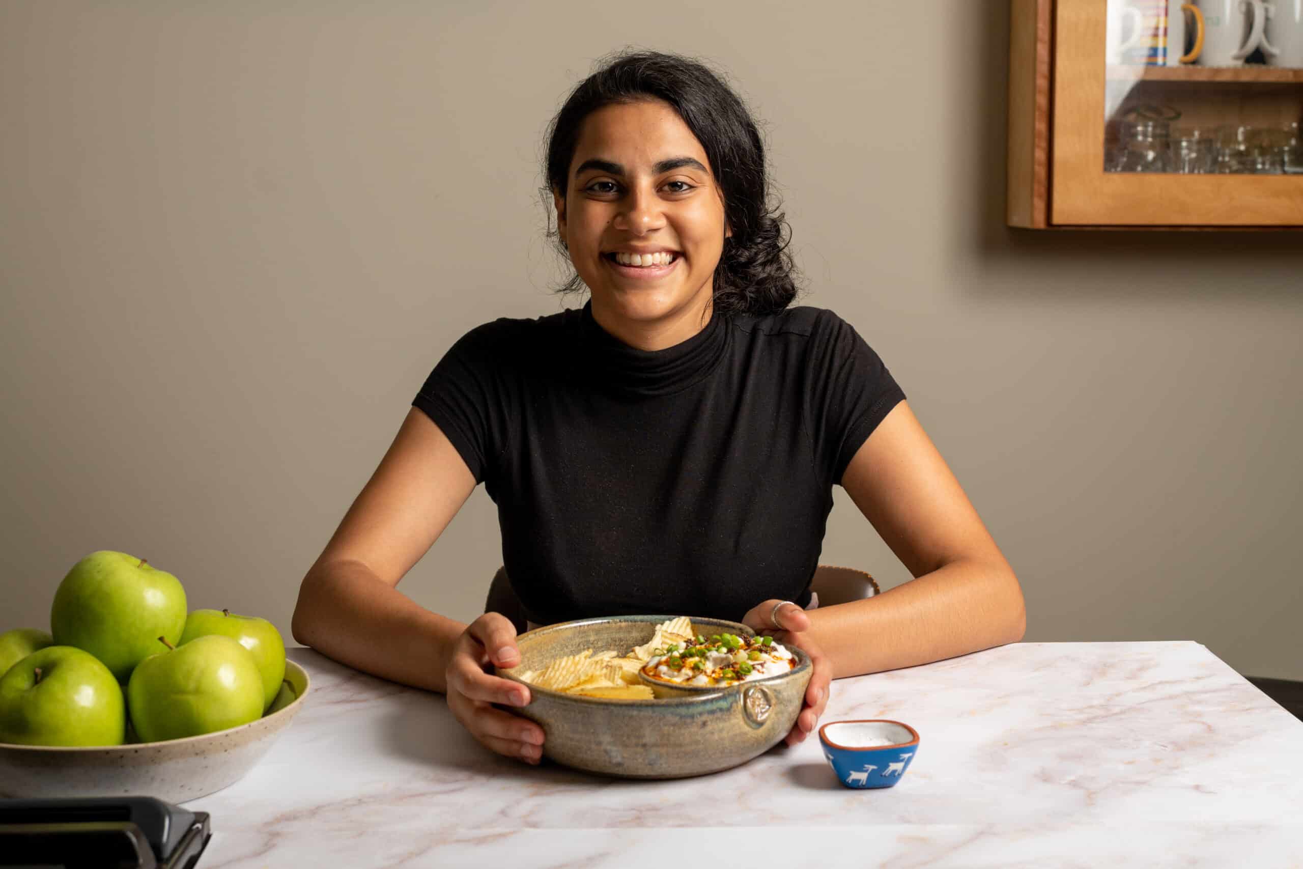 Woman sitting at a kitchen island holding a bowl of chips and dip.