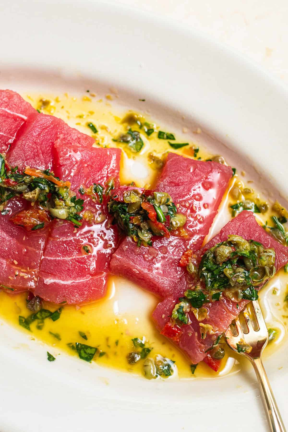 A plate of tuna crudo topped with a caper chili salsa verde in a pool of olive oil.