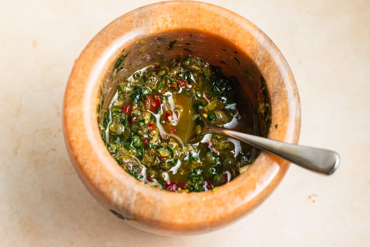 Caper salsa verde with a spoon in a marble mortar and pestle.