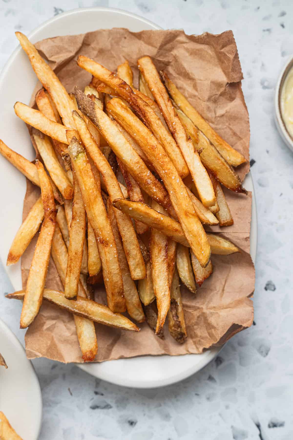 A heap of fries set on a brown paper bag on a plate.