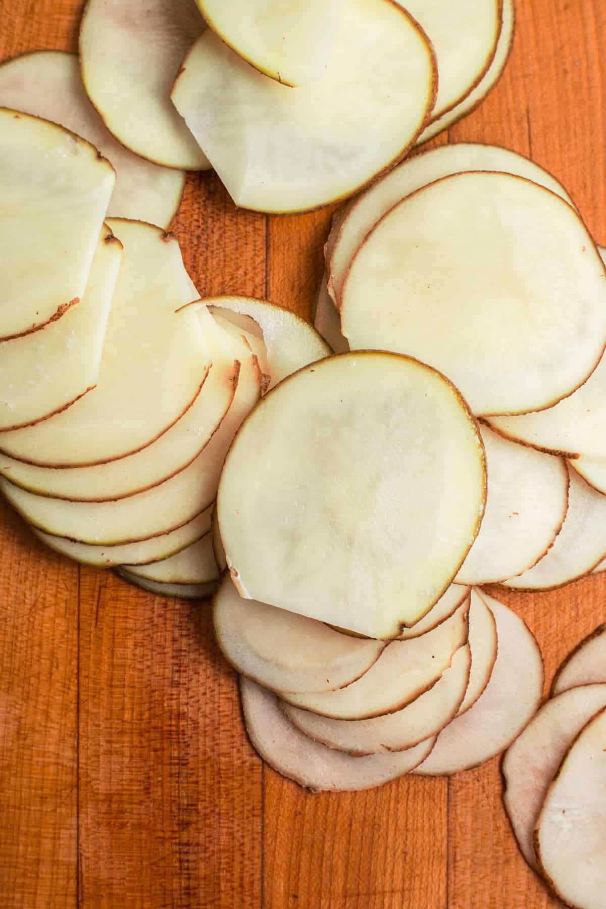 A cutting board with slices of russet potatoes.