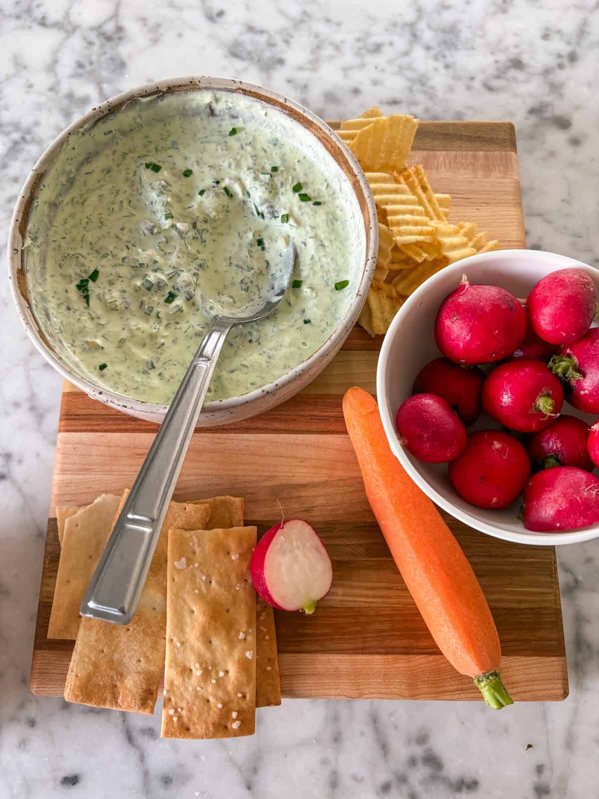 A platter of vegetables, crackers, and chips with a bowl of smoked trout dip in the background.