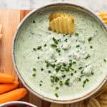 A bowl of smoked trout dip topped with chives and potato chips on a platter of crudites.
