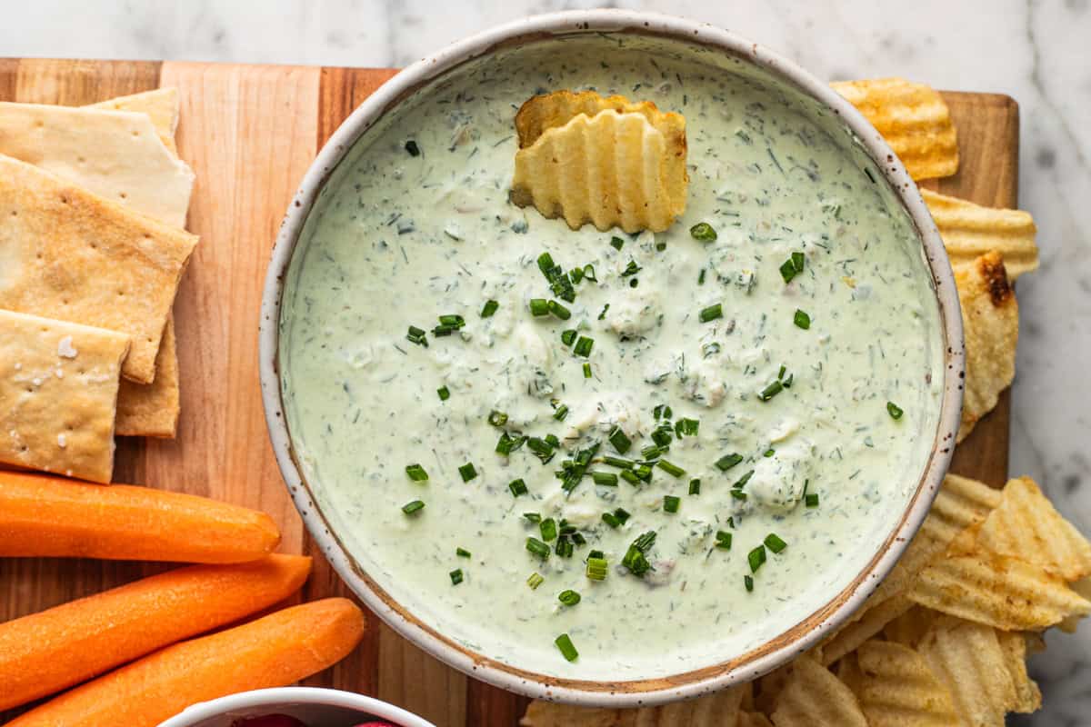 A bowl of smoked trout dip topped with chives and potato chips on a platter of crudites.