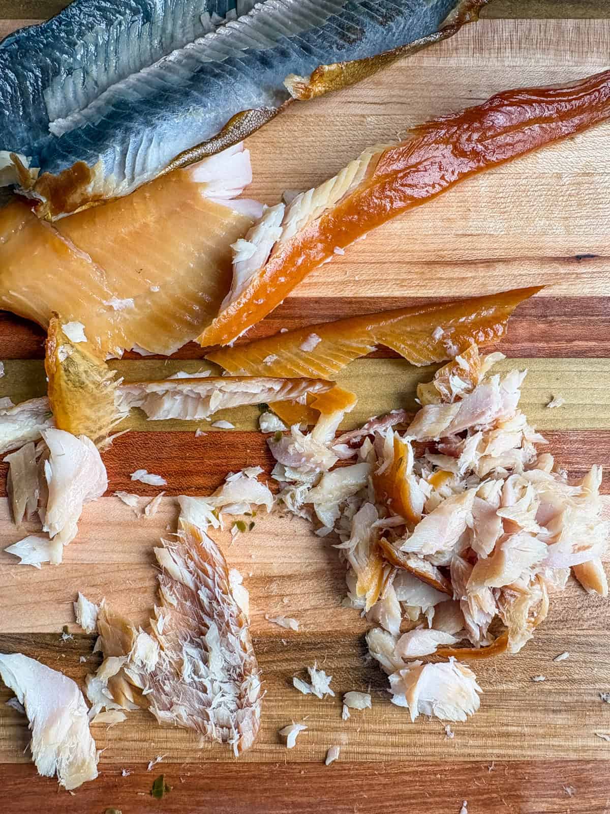 A cutting board with smoked trout being de-skinned and chopped up into small pieces.