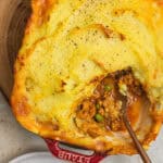 A casserole dish with spiced keema topped with mashed potatoes and a chunk taken out.
