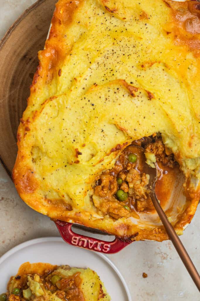 A casserole dish with spiced keema topped with mashed potatoes and a chunk taken out.