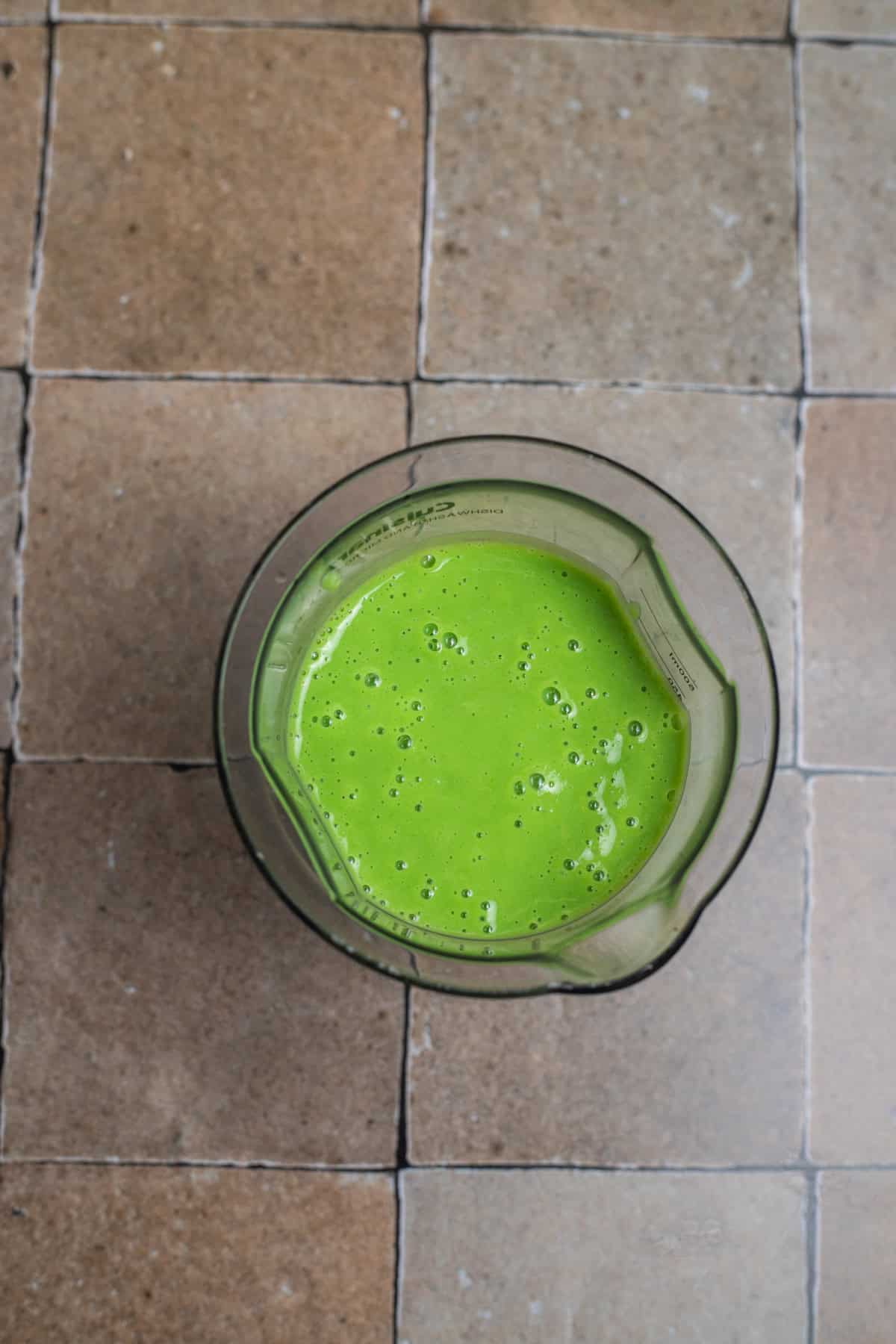 A measuring cup with a green puree in it on a countertop.