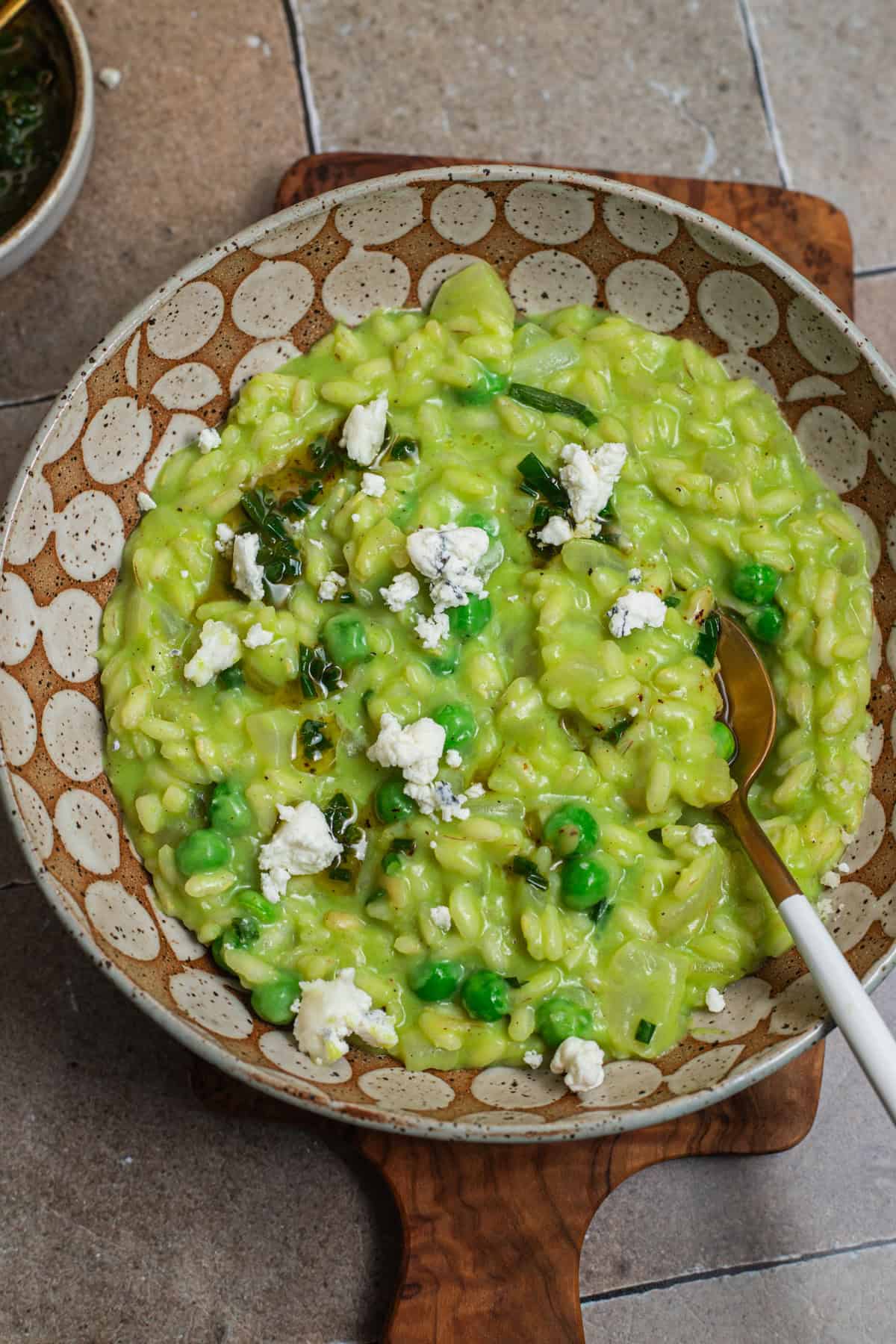 A bowl of risotto in a creamy green sauce topped with peas, brown butter, herbs, and cheese.