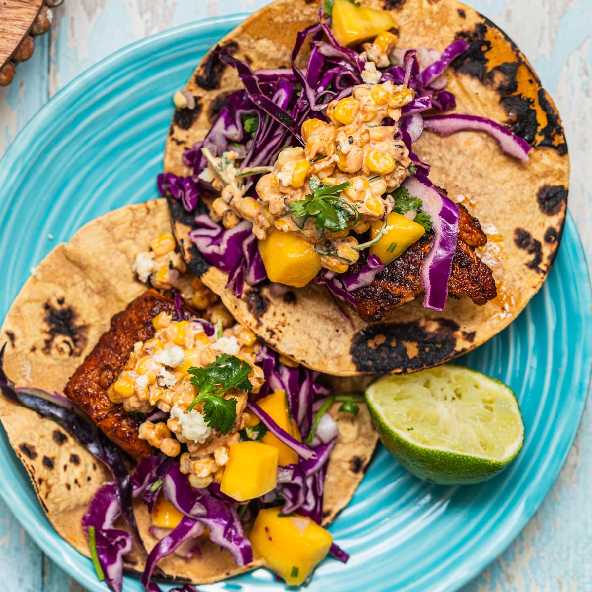 Two fish tacos with cabbage and mango on a plate with a lime.