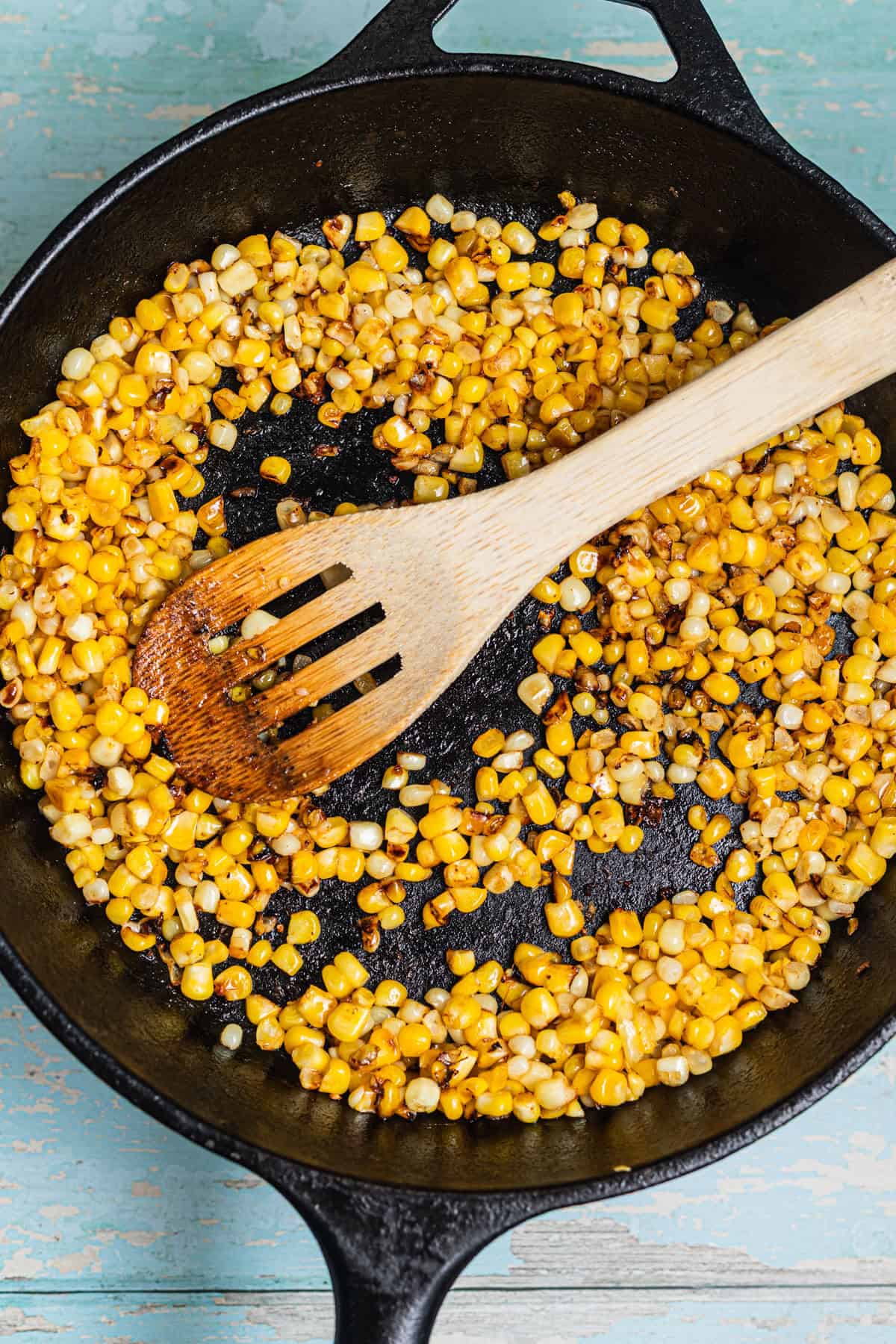 A cast-iron skillet with charred corn and a wooden spoon.