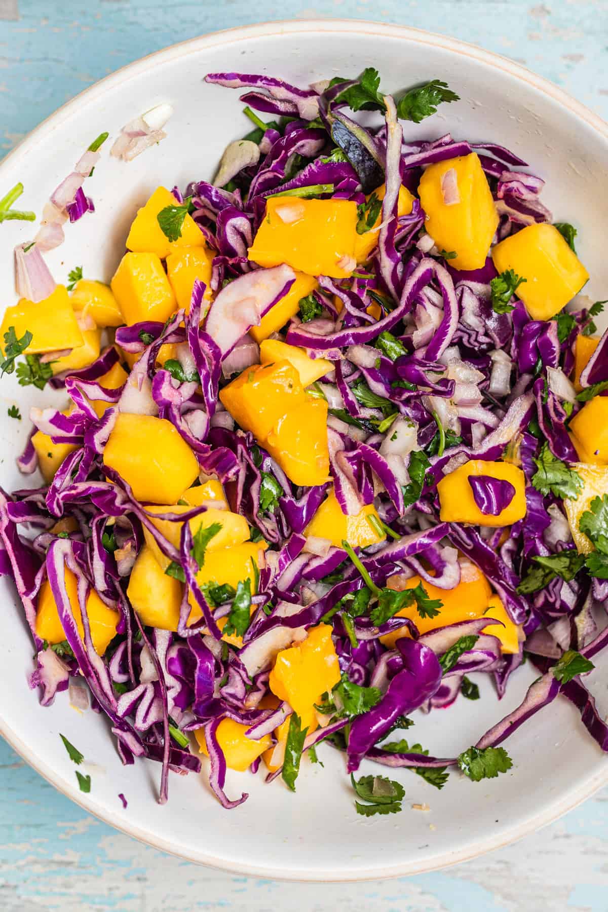 A bowl of mango slaw with purple cabbage and herbs.