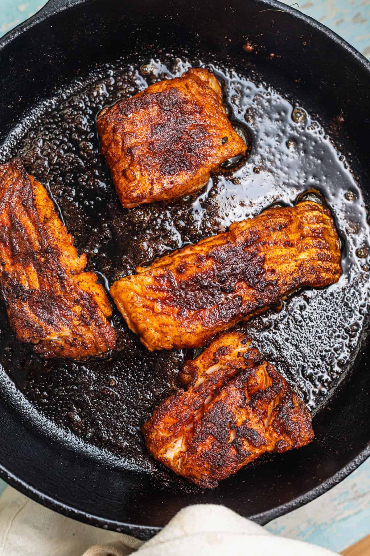 Blackened fish pieces searing in a cast-iron skillet.