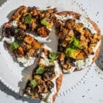 Flatbread pieces with a yogurt sauce and vegetables on a plate with a bowl of za'atar in the background.