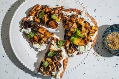 Flatbread pieces with a yogurt sauce and vegetables on a plate with a bowl of za'atar in the background.
