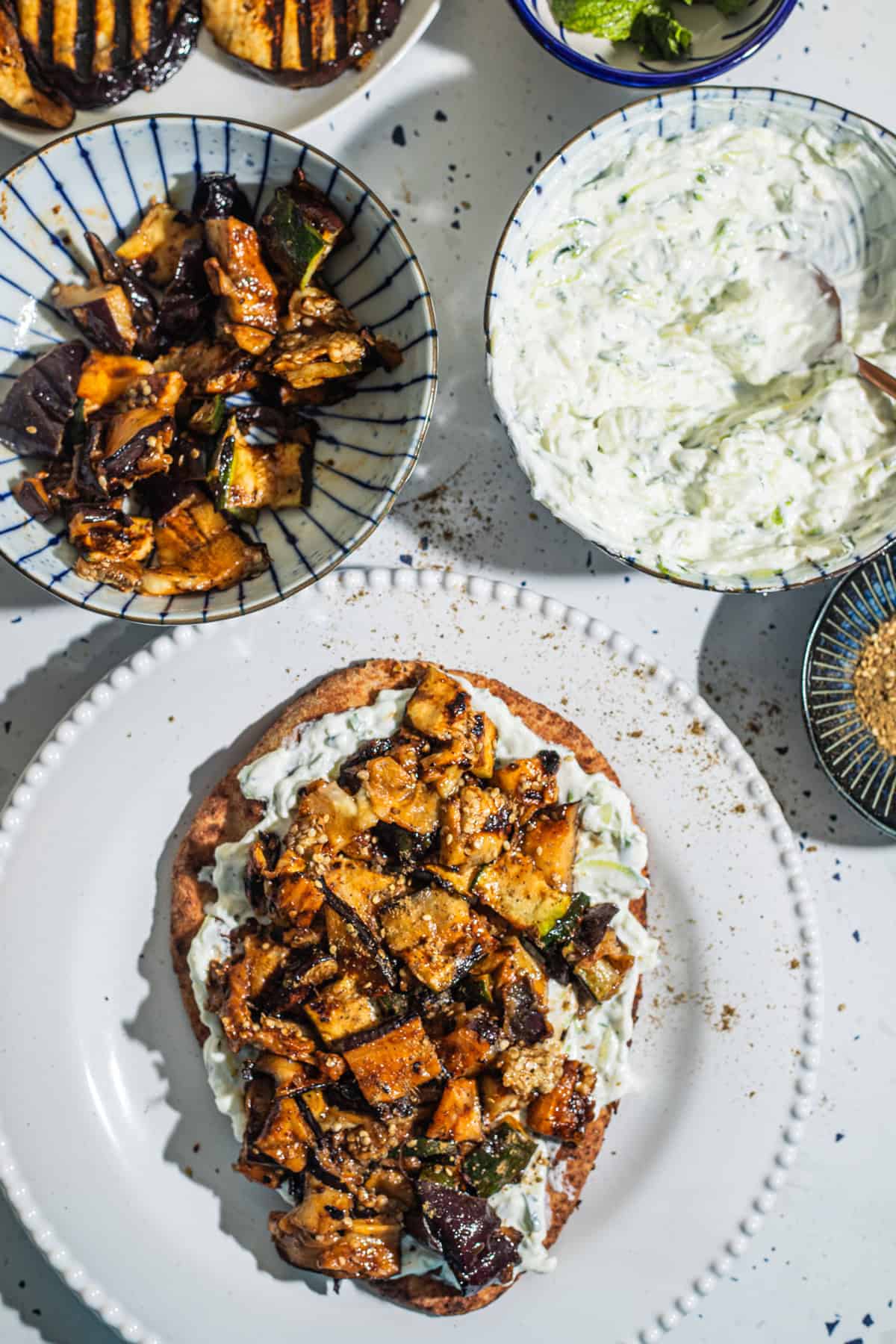 A plate with a vegetable flatbread and various bowls of ingredients in the background.