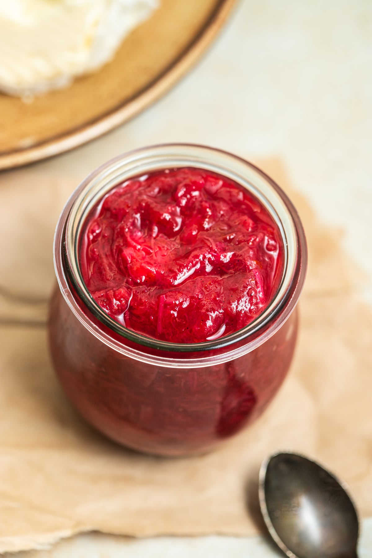 Rhubarb jam in a jar with a spoon and plate of butter in the background.