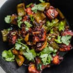 A skillet with chili paneer topped with fresh herbs.