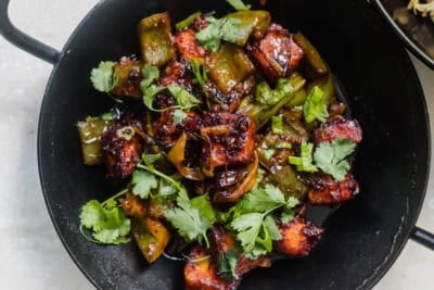 A skillet with chili paneer topped with fresh herbs.