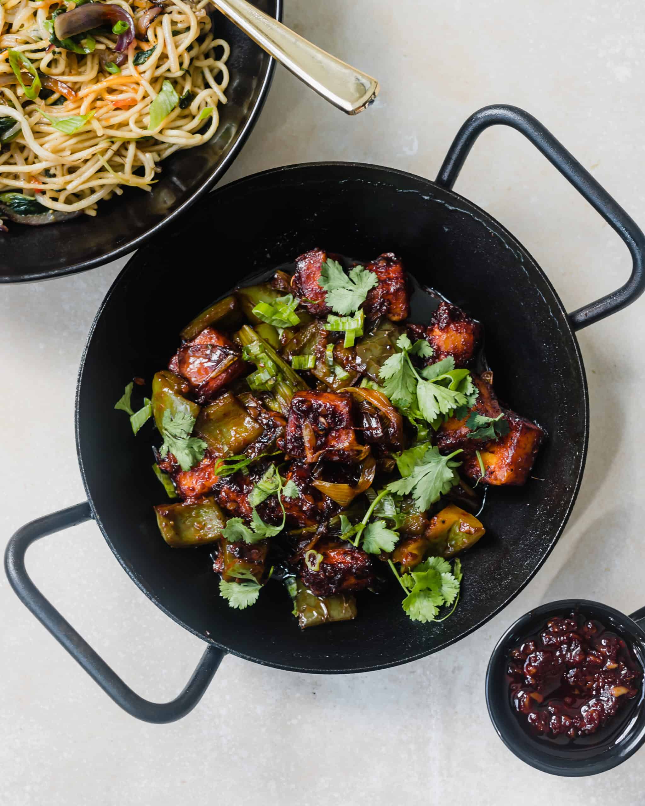 A small skillet with paneer, vegetables, and herbs coated in a spicy sauce.