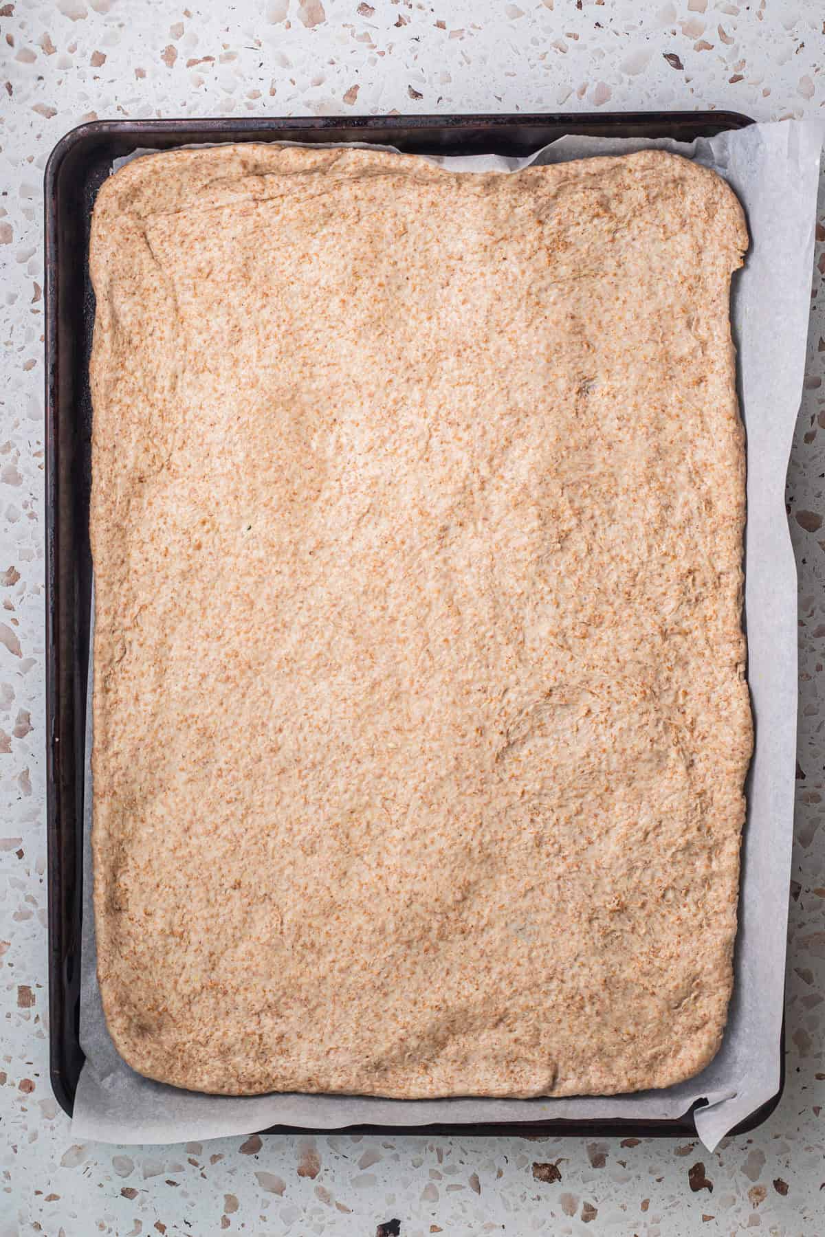 Whole-wheat pizza dough on a parchment-lined baking sheet.