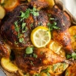 A baking sheet with a roast chicken topped with lemons sitting over a bed of potatoes.