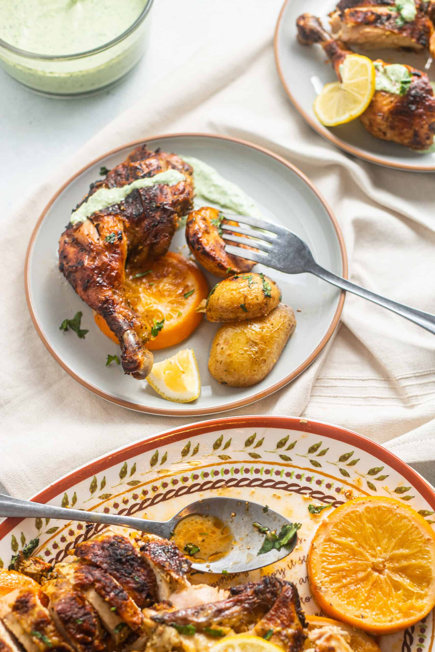 A plate of harissa roast chicken with potatoes and citrus and a larger serving plate in the background.