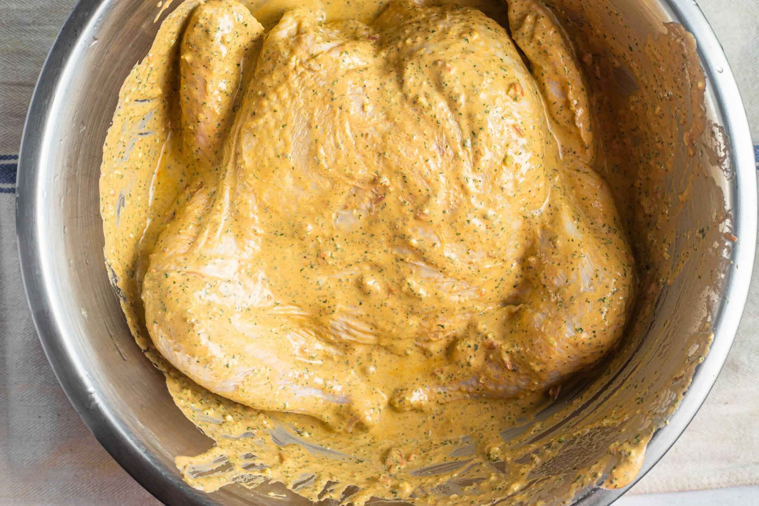 A whole chicken marinated in a spicy yogurt sauce in a metal bowl.